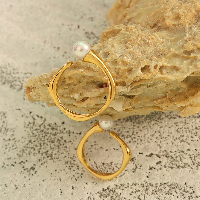 Gold faux pearl open ring displayed in a flat lay with an irregular curved band design