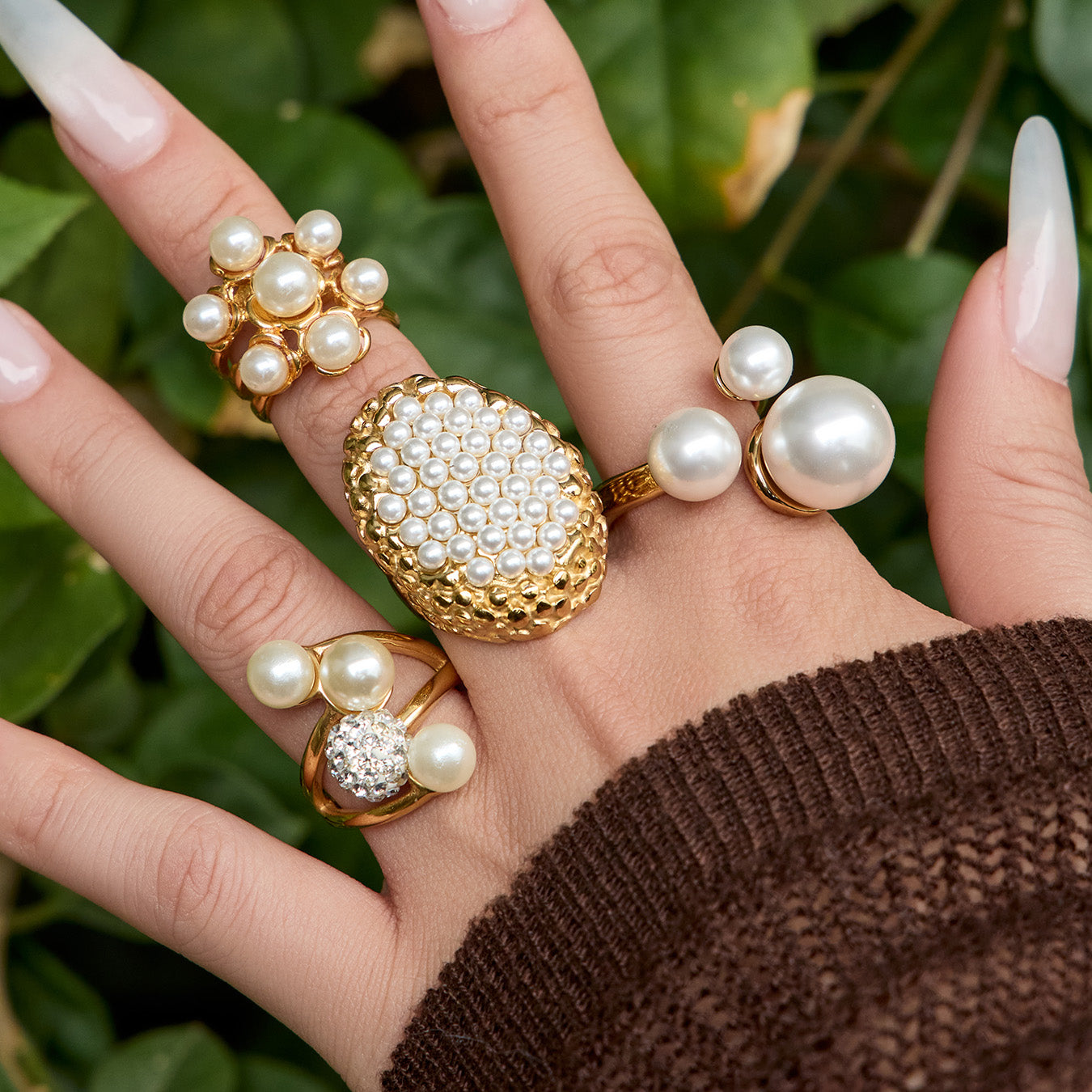 Hand styling oversized faux pearl statement rings against a green background