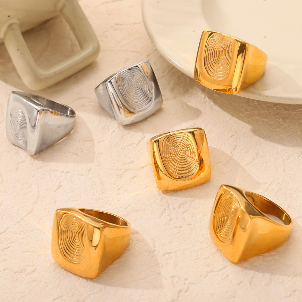Gold and steel fingerprint statement rings arranged together on a neutral jewelry display