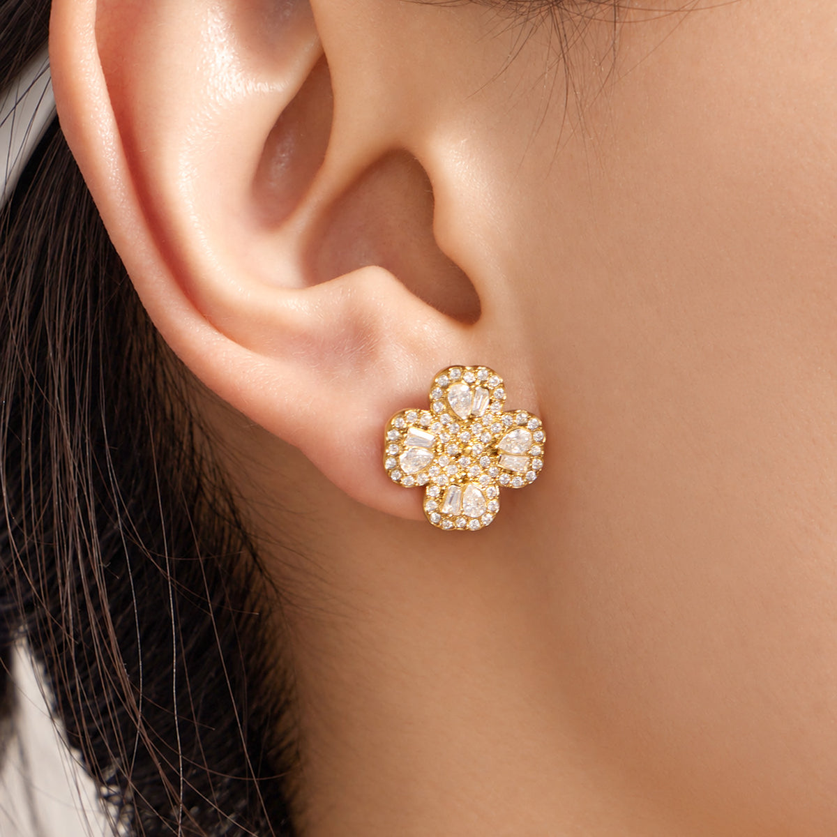 Close-up of gold four-petal flower zircon stud earring worn on ear