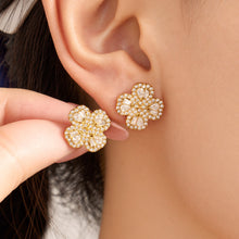 Four-petal flower zircon stud earrings in gold tone shown close-up on model ear