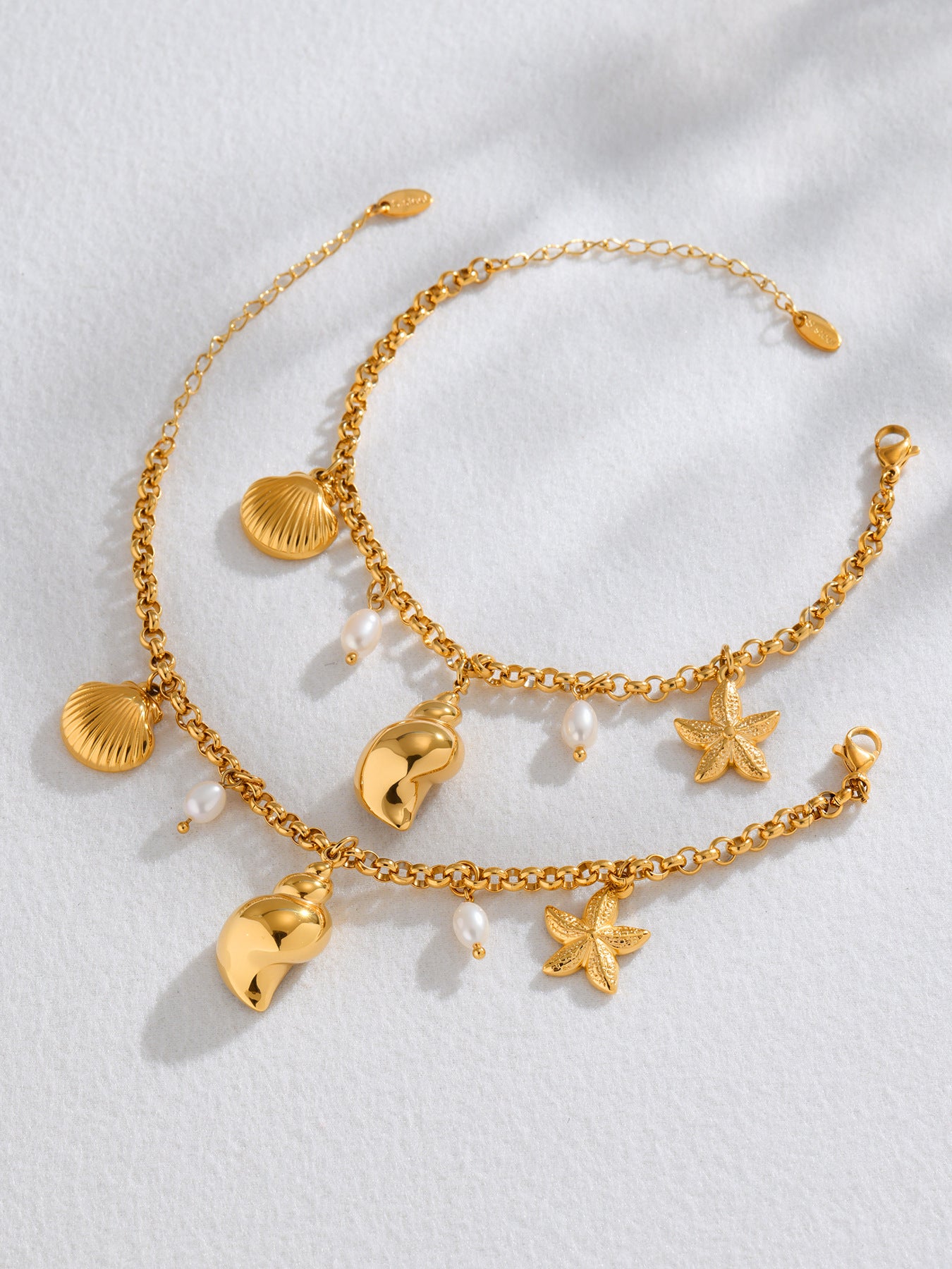 Flat lay of matching freshwater pearl shell charm anklet and bracelet set in 18K PVD gold 316L stainless steel