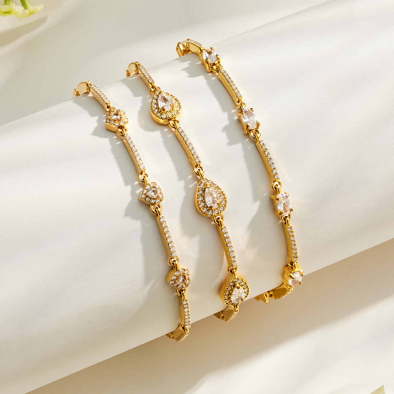 Three gold zircon bracelet styles with heart, square and teardrop motifs displayed together