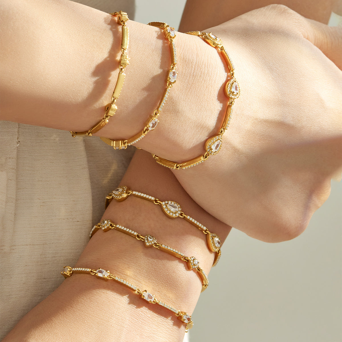 Gold geometric zircon bracelets layered on both wrists with delicate stone-set details