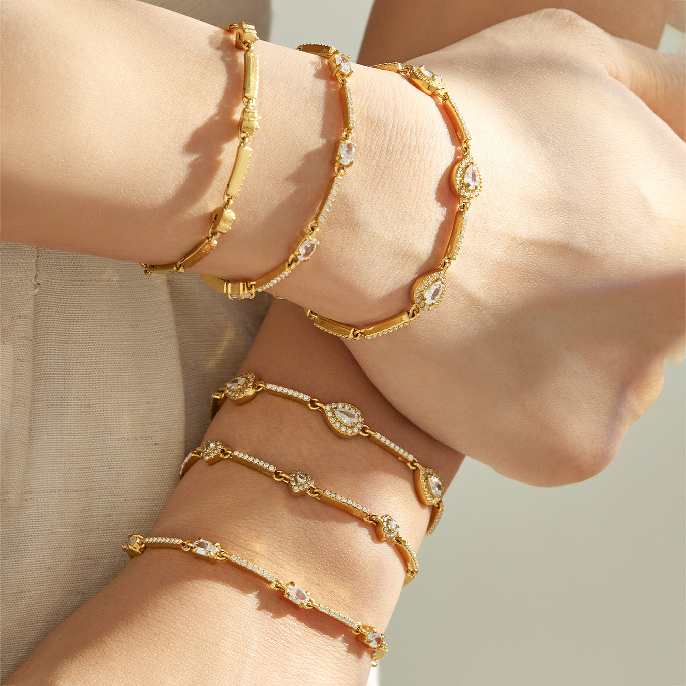 Gold geometric zircon bracelets layered on both wrists with delicate stone-set details