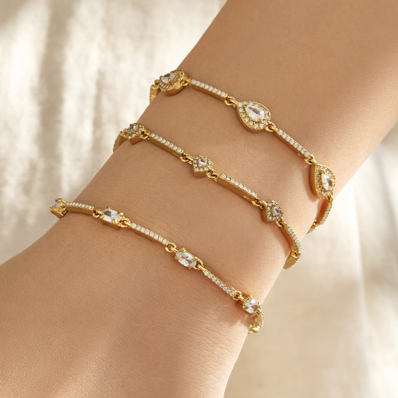 Close-up of gold zircon bracelets with different geometric motifs layered on a model wrist