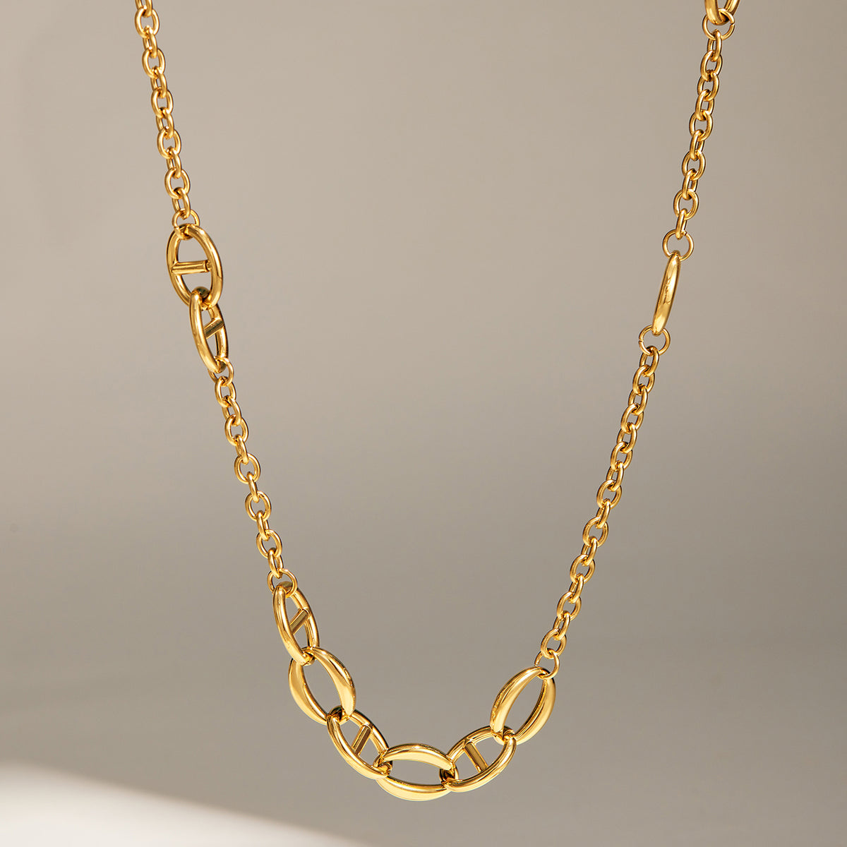 Gold geometric chain necklace showing mixed oval link details on a neutral display