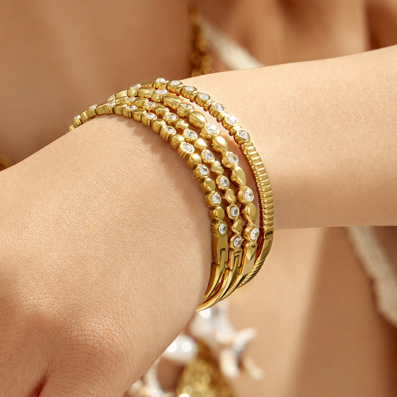 Close-up of layered gold geometric zircon bangles worn on a model wrist