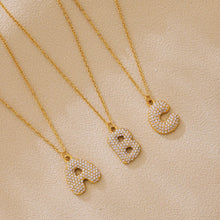 Gold A B and C iced out initial letter necklaces with zircon pave pendants on beige flatlay background