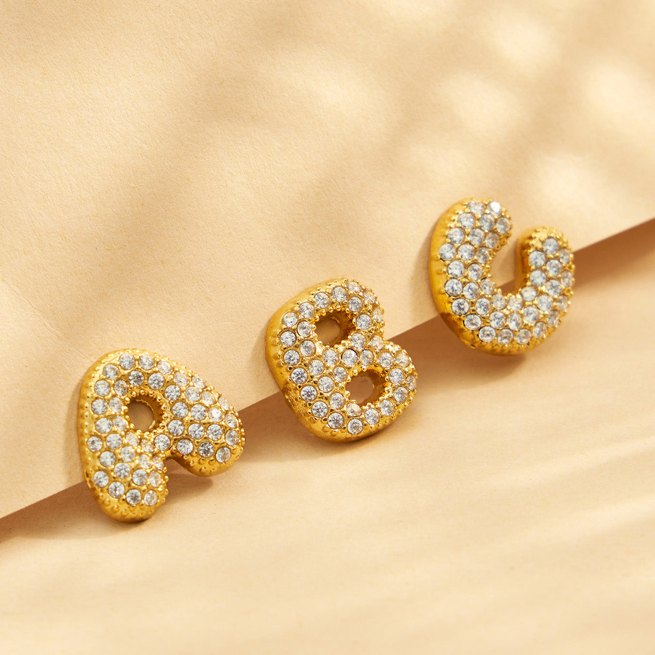 Close-up of pavé gold A, B and C initial stud earrings