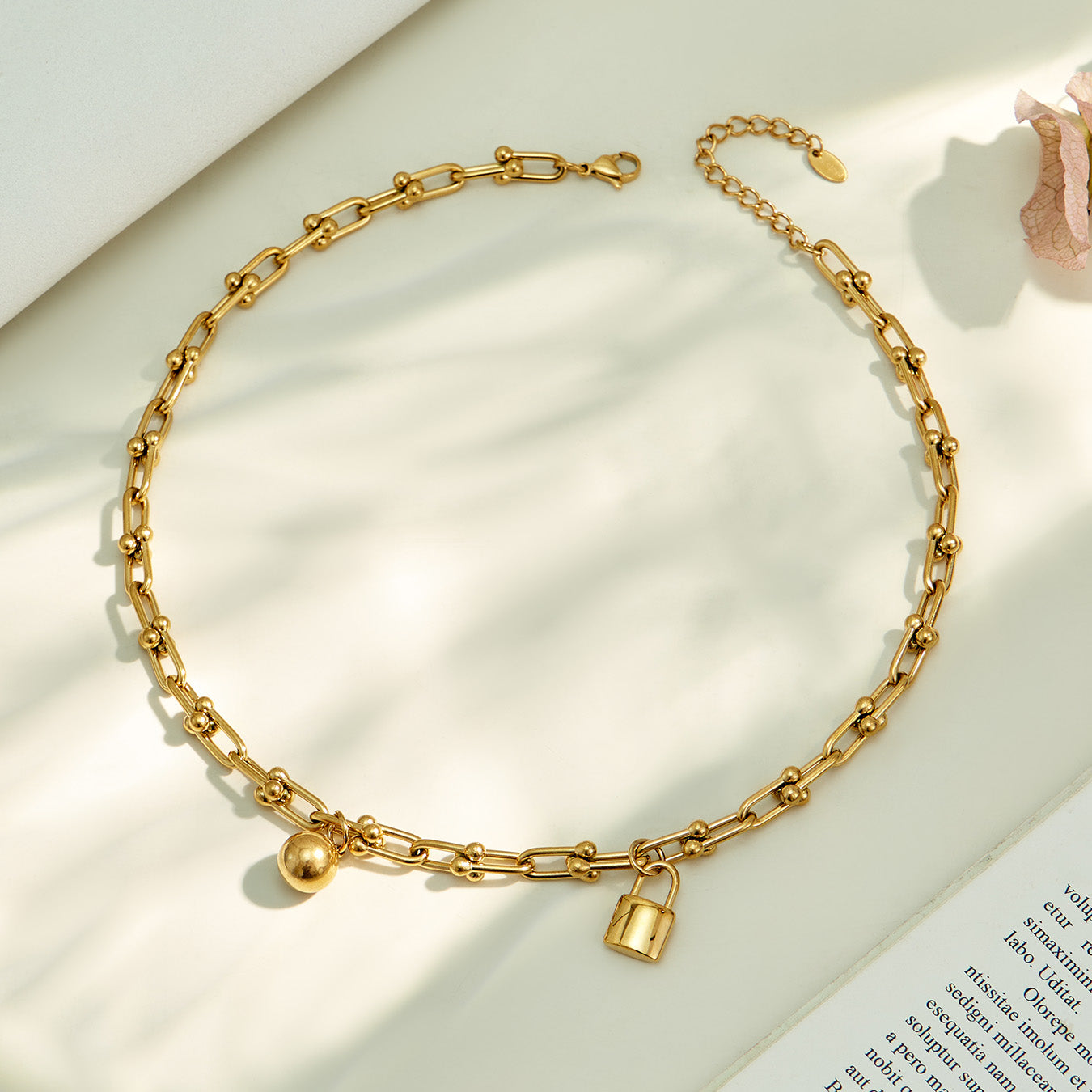 Gold ball lock chain link necklace arranged in a circular flat lay on neutral fabric