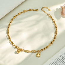 Gold ball lock chain link necklace arranged in a circular flat lay on neutral fabric