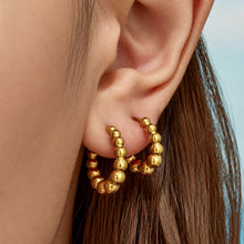 Close-up of a model wearing layered gold beaded hoop earrings