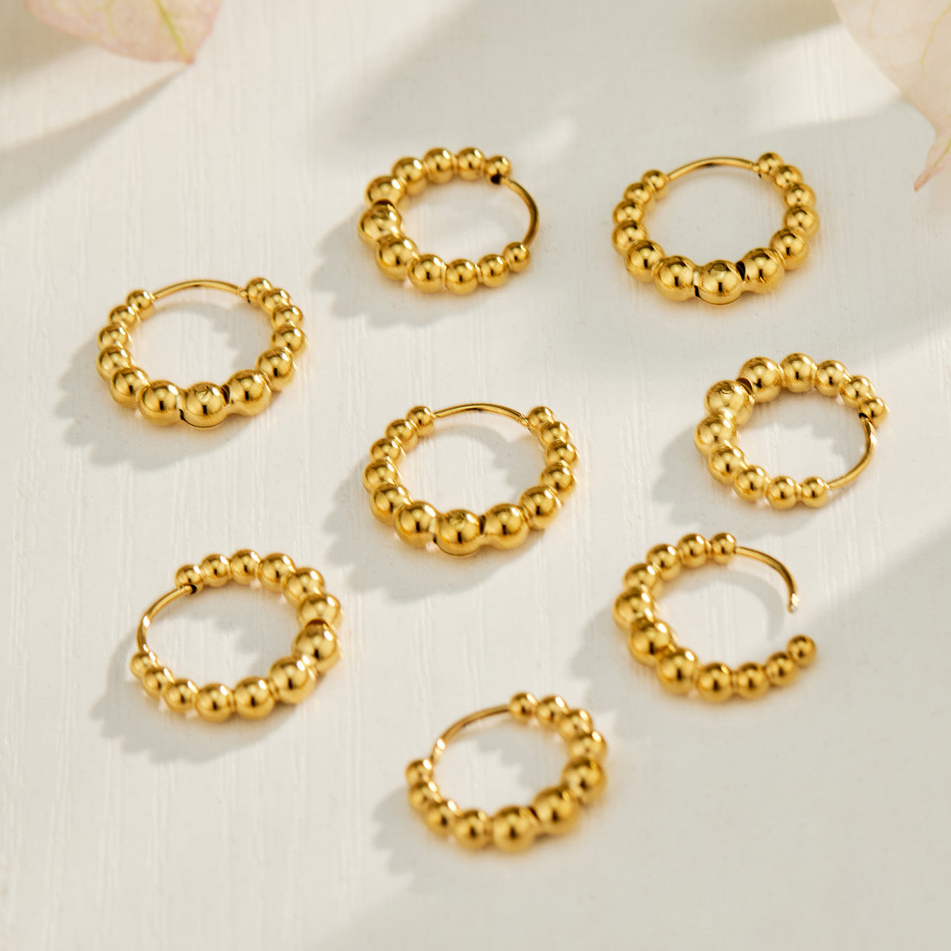 Multiple pairs of gold beaded hoop earrings arranged in a circular flat lay