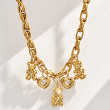 Gold teddy bear and heart charm necklace arranged in a circular flat lay