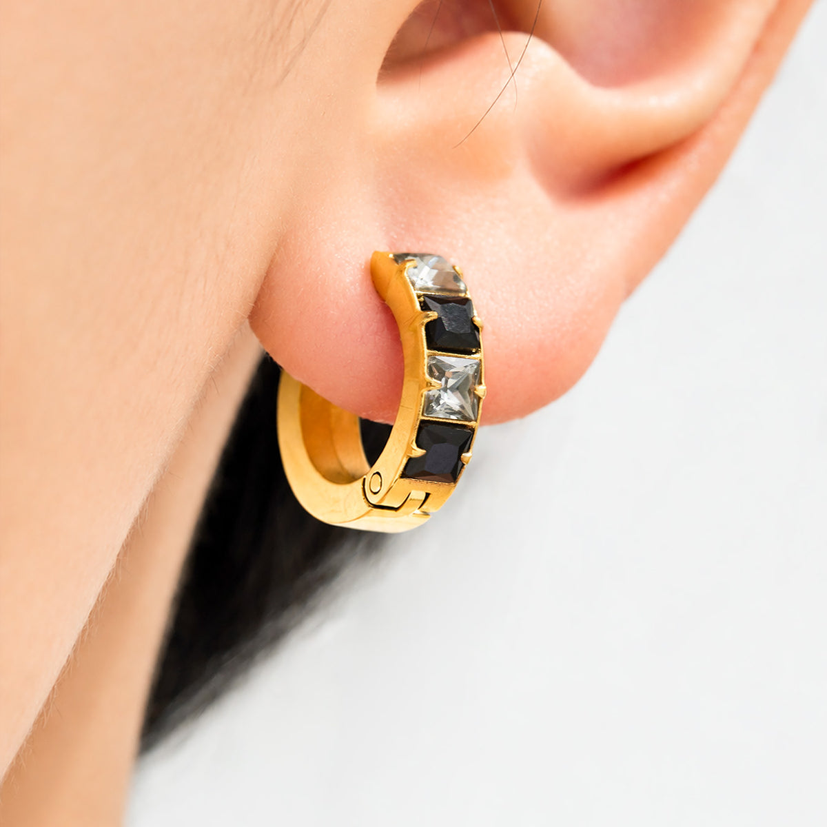Gold-tone stainless steel hoop earring with black CZ accents worn on ear
