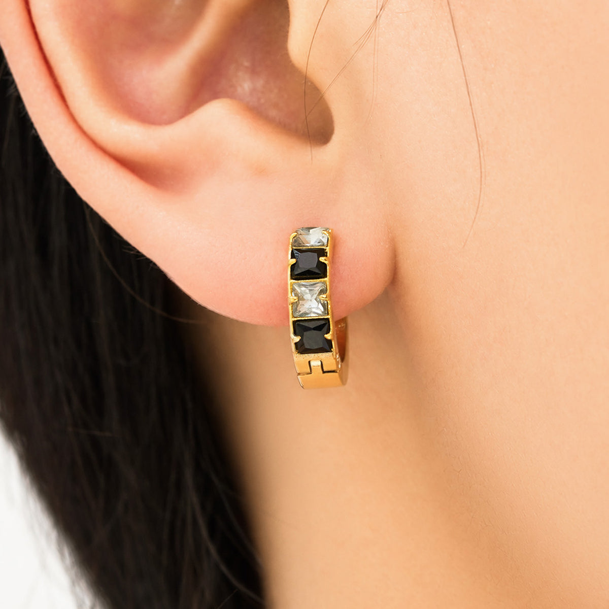 Black cubic zirconia gold-tone huggie earring shown close up on ear