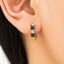 Black cubic zirconia gold-tone huggie earring shown close up on ear