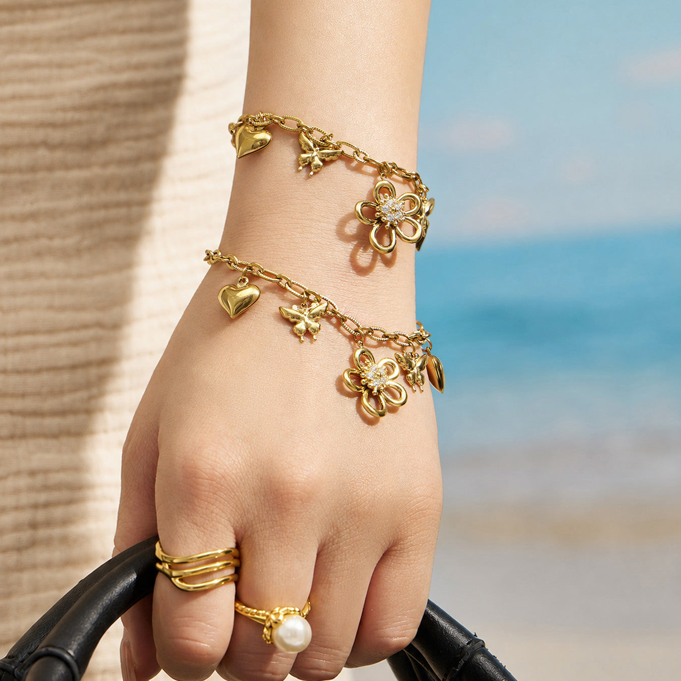 Gold butterfly and flower charm bracelet worn on the wrist in a beach setting