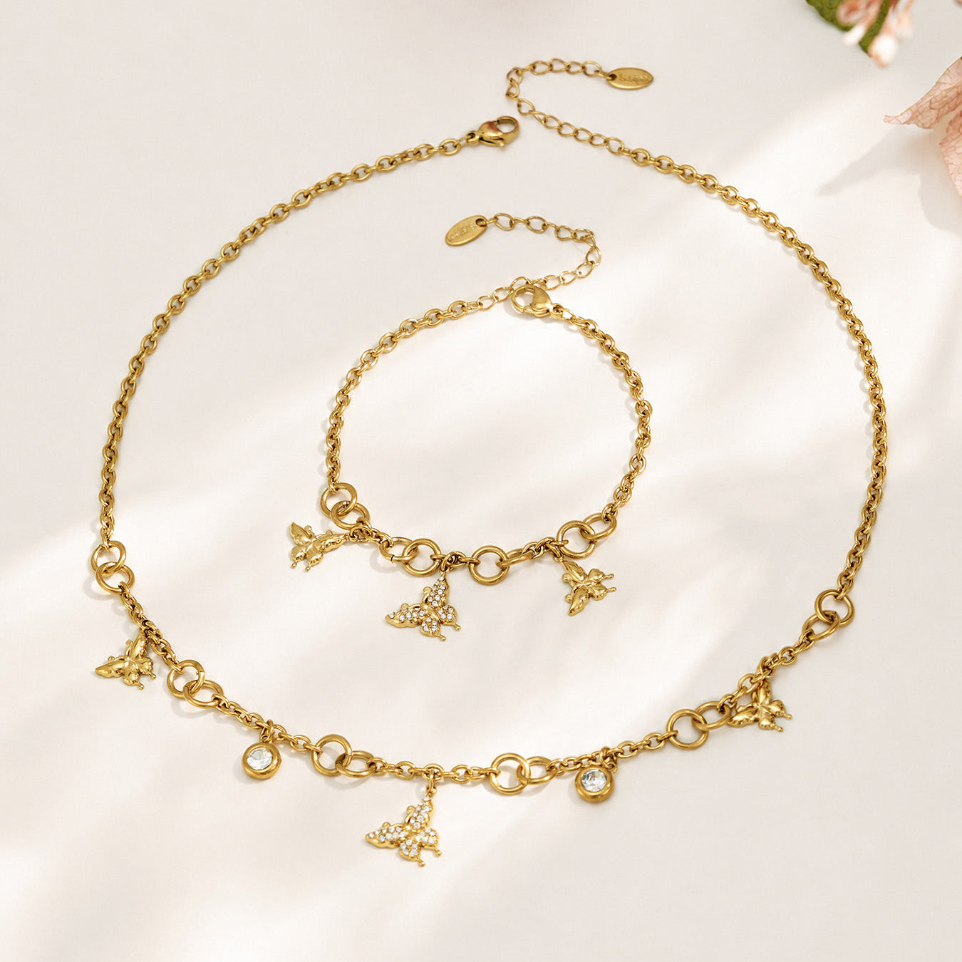 Gold butterfly charm necklace and bracelet arranged together in a circular flat lay