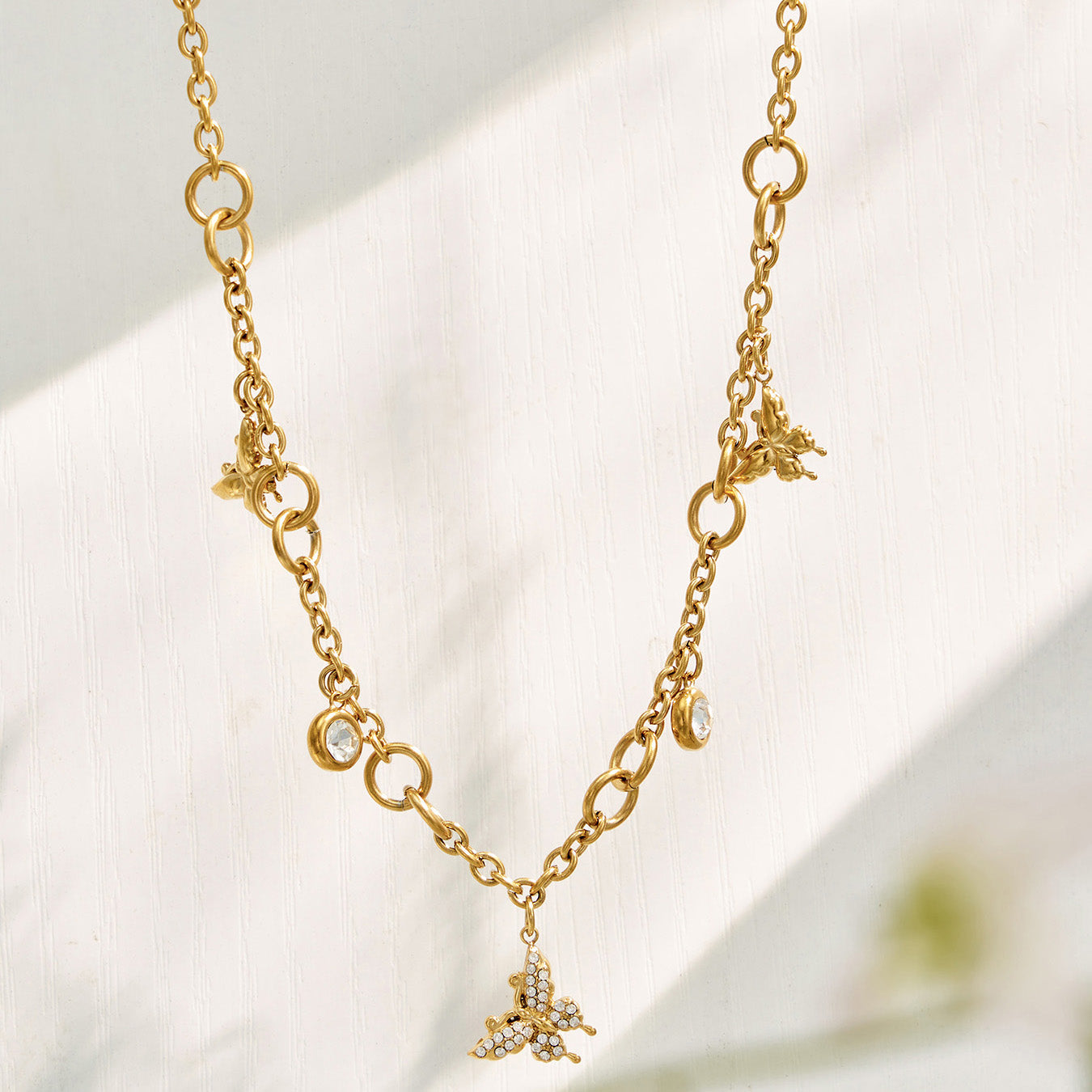 Gold butterfly zircon necklace with delicate dangling charms displayed on white