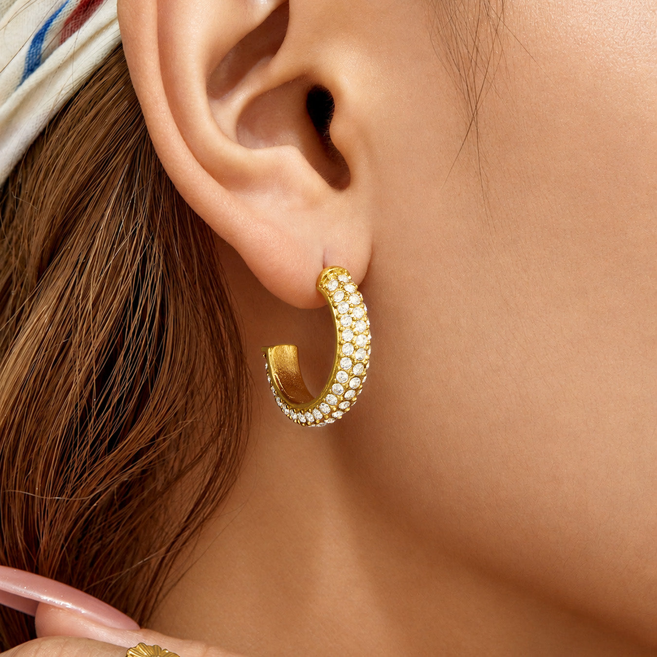 Close-up of gold C-shaped cubic zirconia hoop earrings worn on the ear