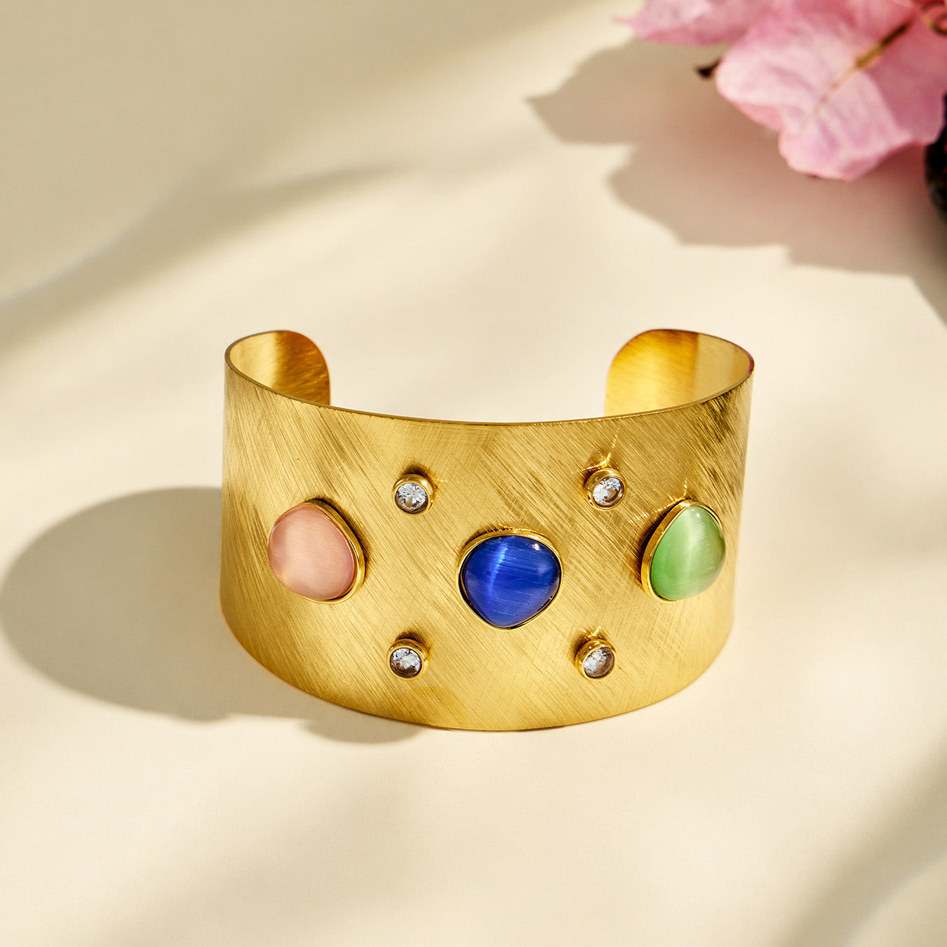 Front product detail of a brushed gold cuff bracelet with blue, green and pink stones