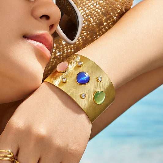 Close-up of a model wearing a gold cuff bracelet with blue, green and pink cat-eye effect stones