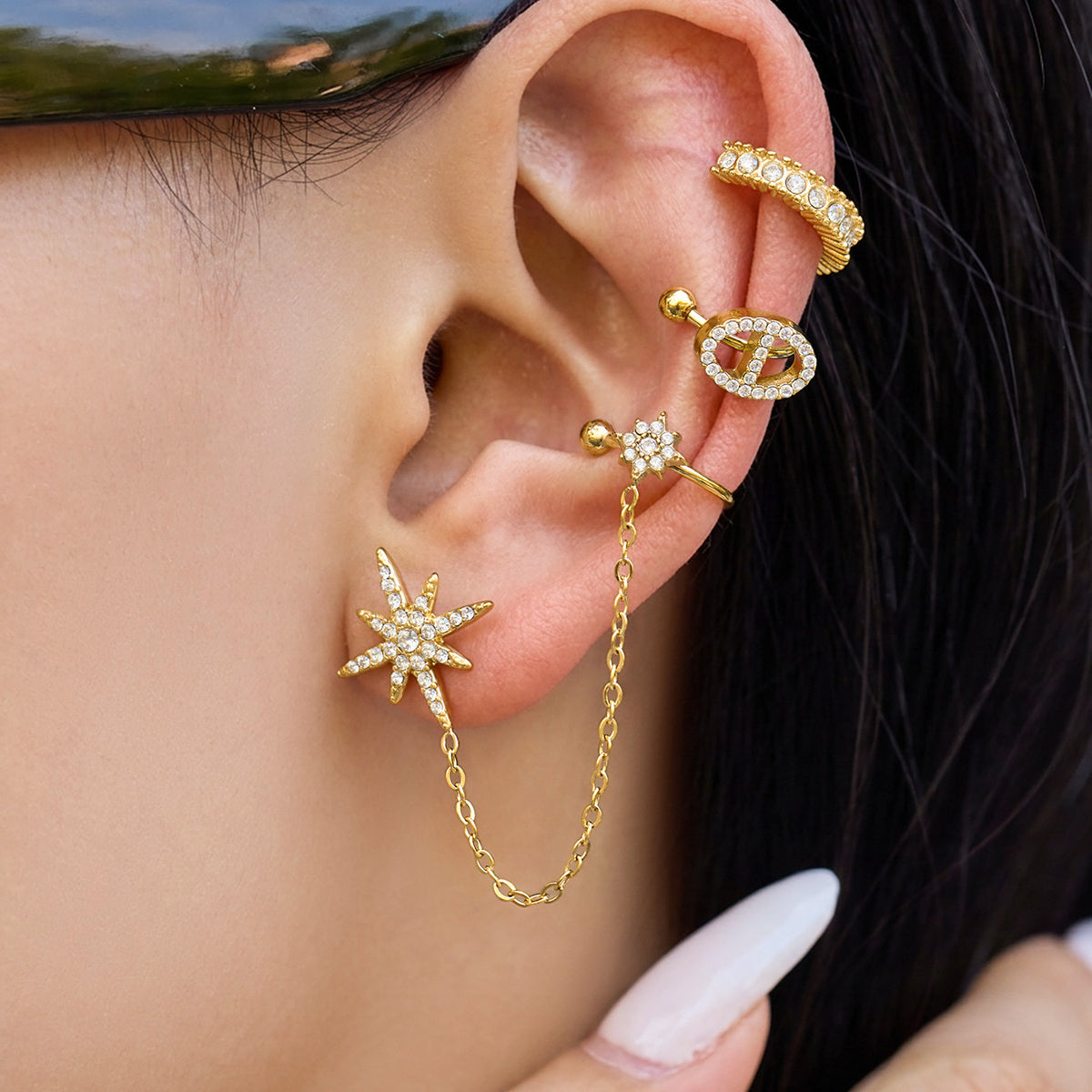 Model styling a gold starburst chain ear accessory with additional gold ear jewelry for a layered ear look