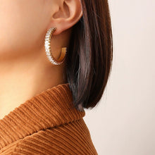 Model wearing gold C-shaped hoop earrings with clear cubic zirconia accents