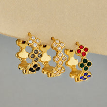 Close-up of gold clover huggie earrings with white, multicolor and black CZ details