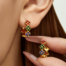 Hand holding gold multicolor clover huggie earrings beside the ear