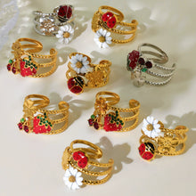Gold-tone colorful enamel statement rings with floral, ladybug and strawberry designs arranged in a jewelry display