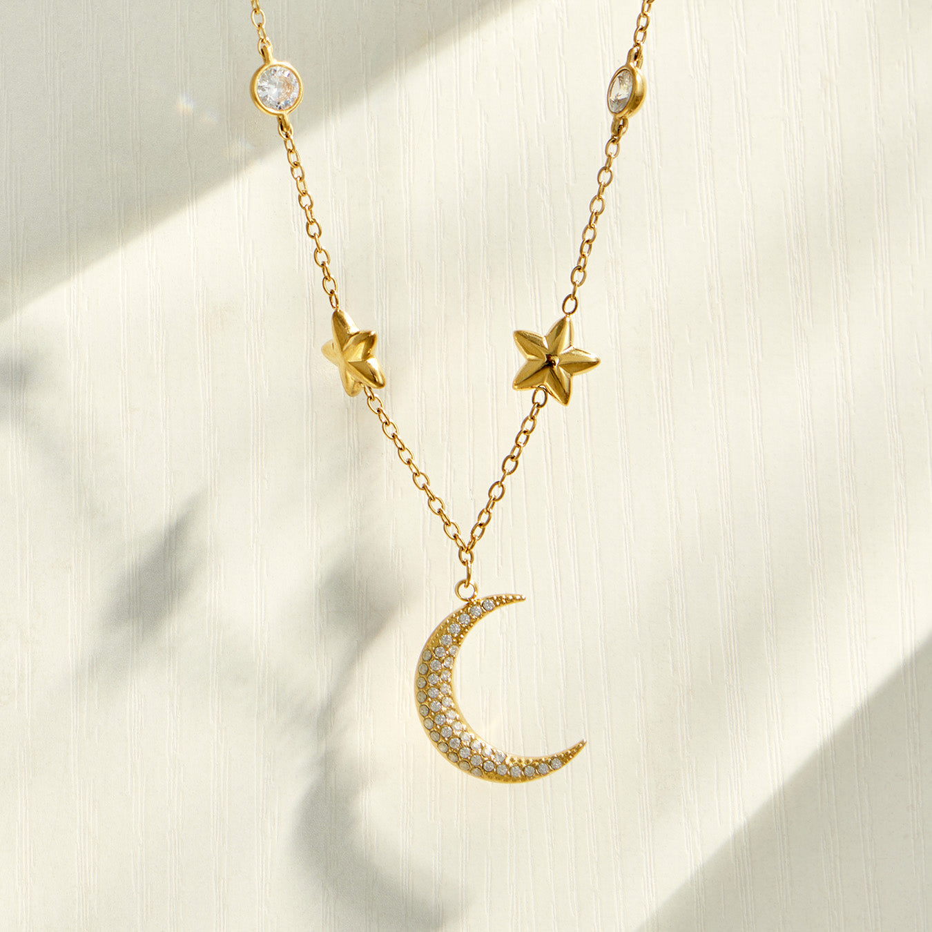 Gold crescent moon necklace with delicate star charms displayed on neutral fabric