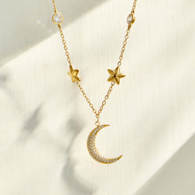 Gold crescent moon necklace with delicate star charms displayed on neutral fabric