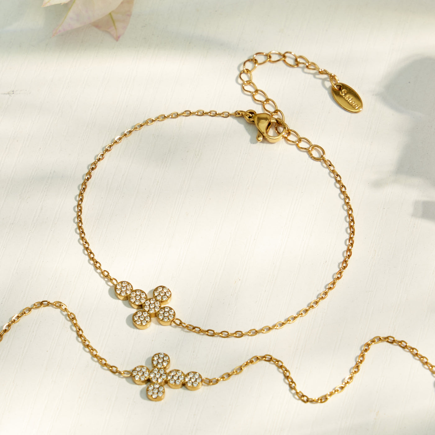 Gold cross zircon necklace and bracelet options arranged on a soft ivory surface