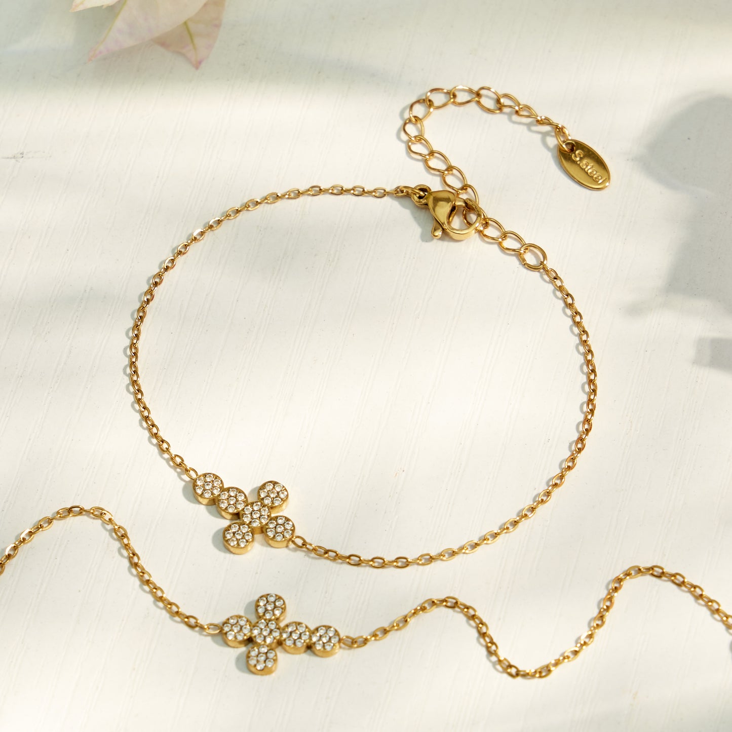 Gold cross zircon necklace and bracelet options arranged on a soft ivory surface