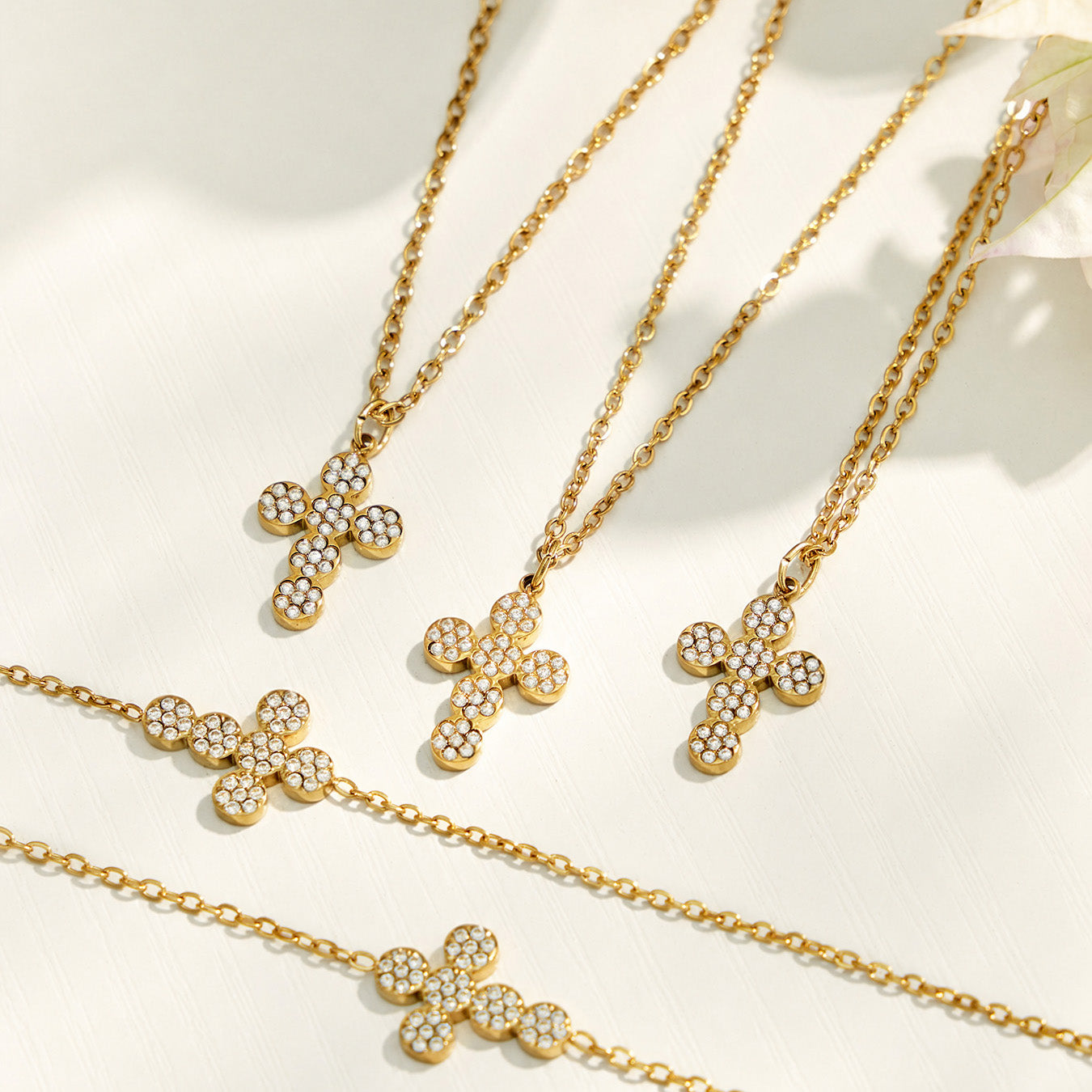 Three gold cross zircon pendant necklaces arranged on a light neutral background