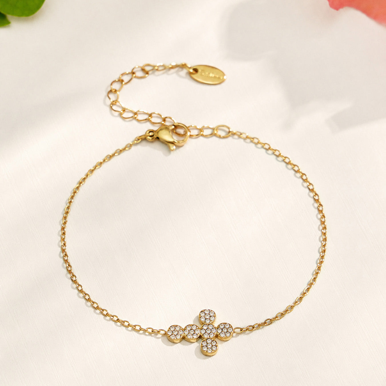 Gold chain bracelet with a clear zircon cross centerpiece on a neutral background
