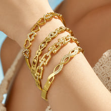Model wearing multiple gold cubic zirconia bangles across both wrists