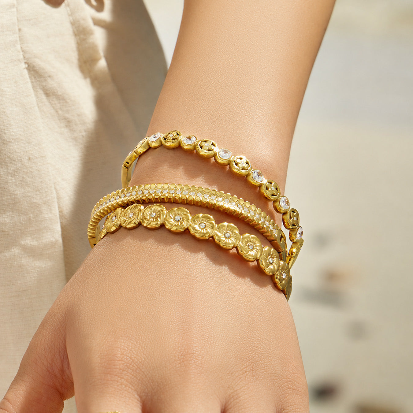Front view of a model wearing three gold-tone cubic zirconia bangles