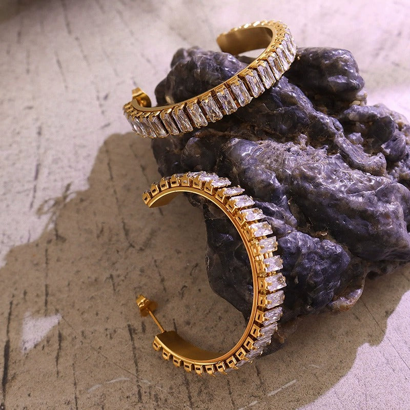 Close-up of gold C-shaped cubic zirconia hoop earrings showing the stone setting and curved profile