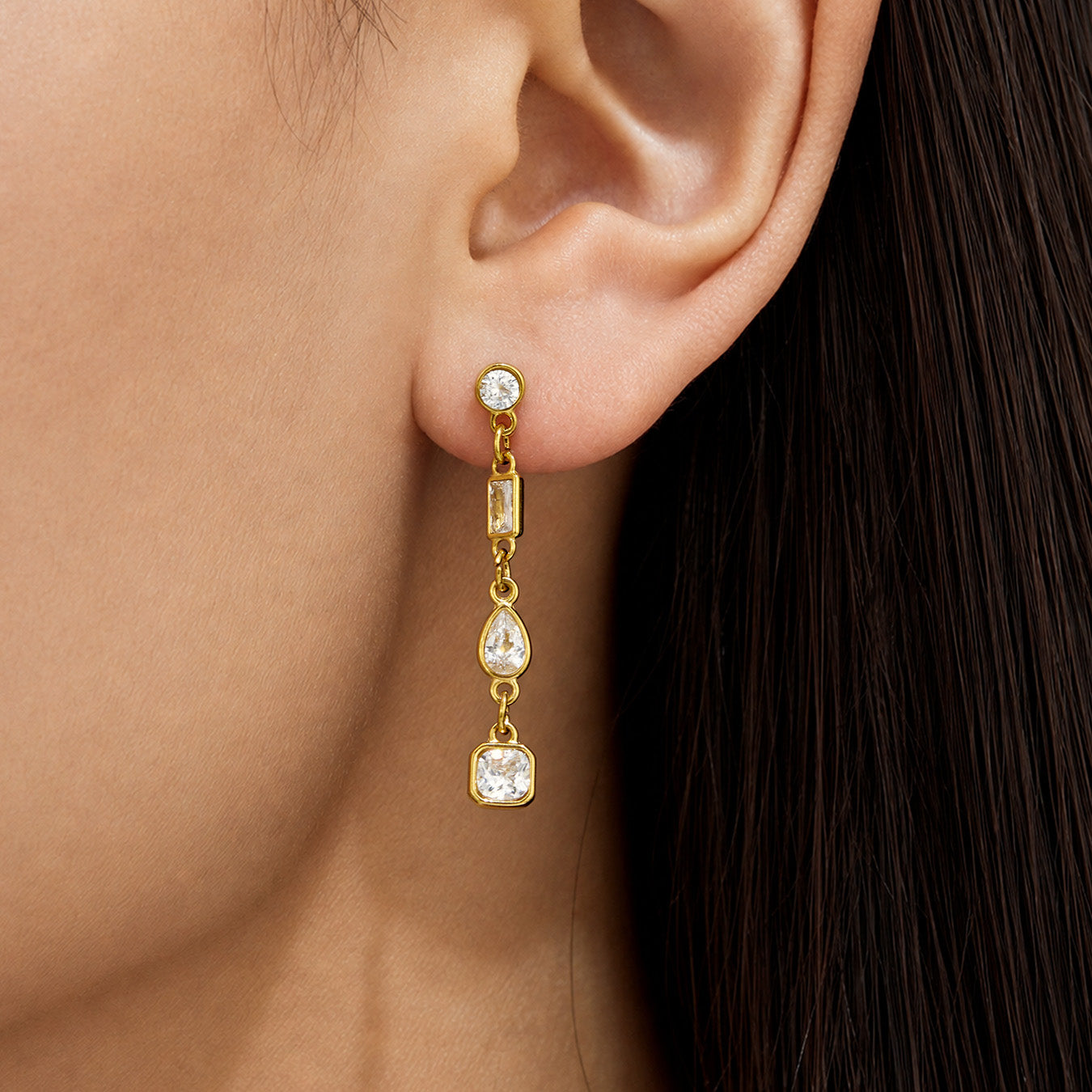 Close-up of gold cubic zirconia dangle earrings worn on the ear