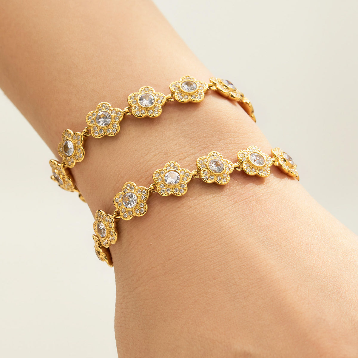 Gold-tone cubic zirconia flower link bracelets shown close up together on the wrist