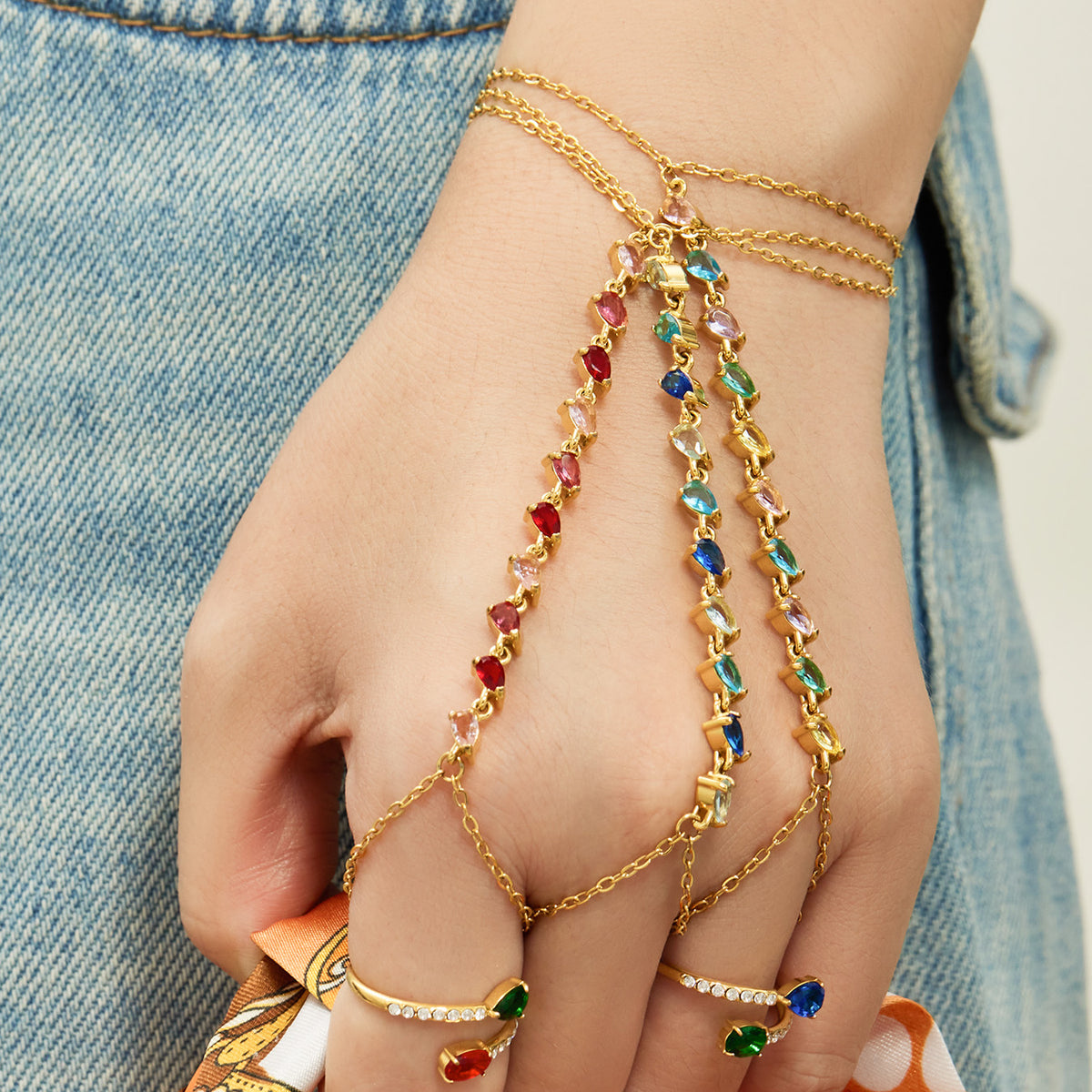 Gold-tone stainless steel CZ hand chain bracelets layered across the hand with red and blue stones