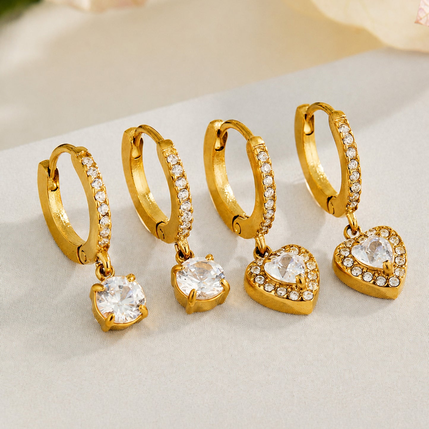 Gold cubic zirconia huggie earrings displayed in heart and round charm styles