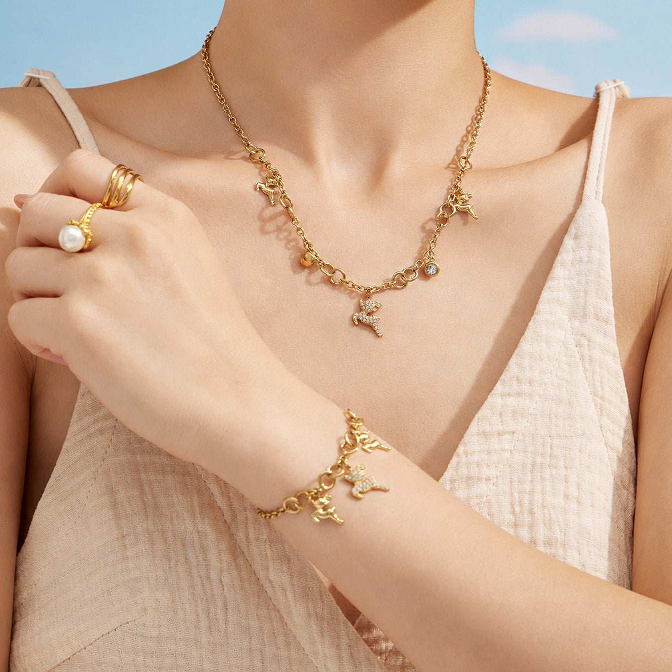 Model wearing a gold deer charm necklace and coordinating bracelet with a white outfit