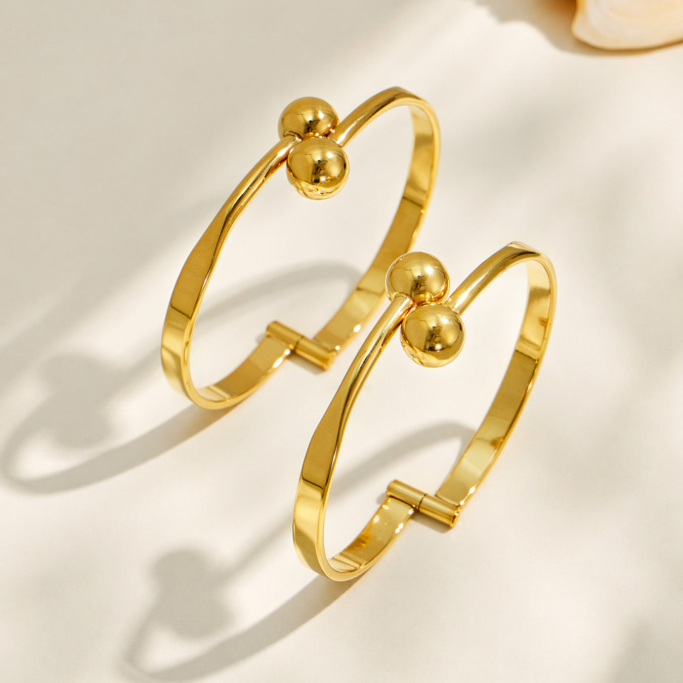 Side-angle view of a gold double ball cuff bracelet showing its open cuff structure