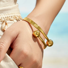 Gold double ball cuff bracelet stacked with minimalist bracelets on a model wrist