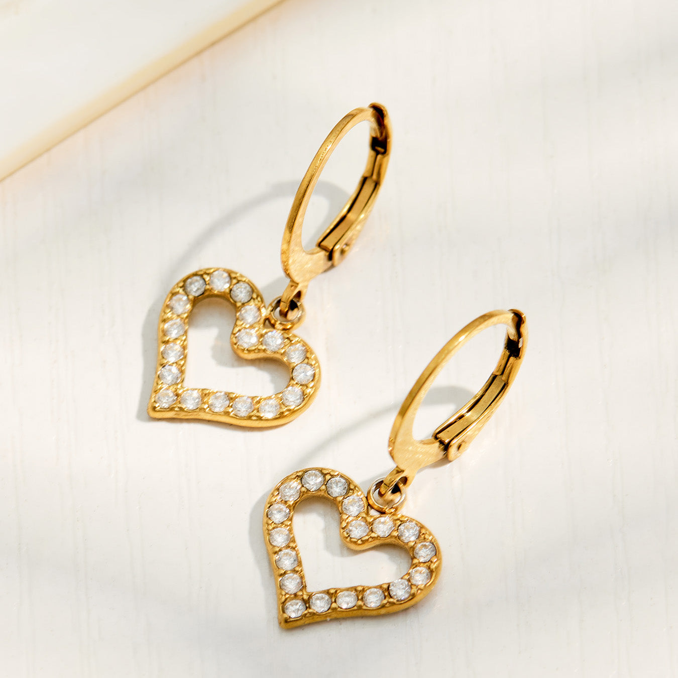 Gold double heart cubic zirconia earrings in a styled flat lay